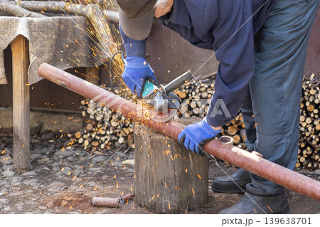 Craftsman using an angle grinder to cut a metal pipe outdoors, generating sparks and showing industrial labor, craftsmanship, maintenance, metalwork, construction, and repair task Craftsman using an angle grinder to cut a metal pipe outdoors, generating sparks and showing industrial labor, craftsmanship, maintenance, metalwork, construction, and repair task 139638701