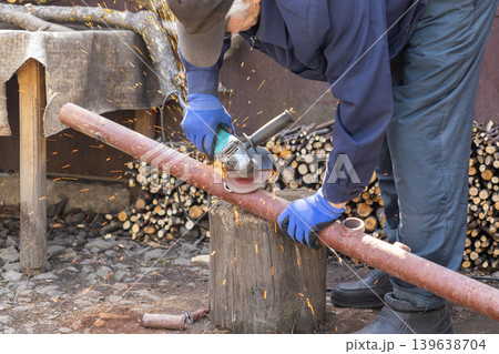 Craftsman using an angle grinder to cut a metal pipe in a backyard, emphasizing heavy industry work, precise manual labor, home improvement, and professional maintenance tasks Craftsman using an angle grinder to cut a metal pipe in a backyard, emphasizing heavy industry work, precise manual labor, home improvement, and professional maintenance tasks 139638704
