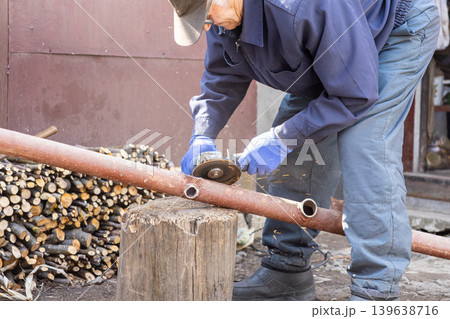 Senior man cutting metal pipe with an angle grinder, performing home improvement and repair work in a backyard, illustrating DIY construction skills and manual labor maintenance Senior man cutting metal pipe with an angle grinder, performing home improvement and repair work in a backyard, illustrating DIY construction skills and manual labor maintenance 139638716