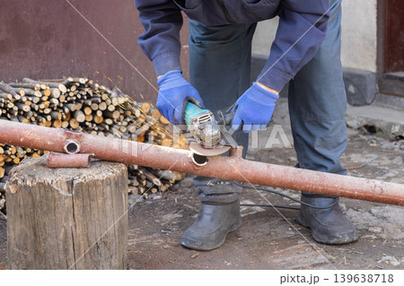 A professional construction worker uses a powerful angle grinder to cut a metal pipe, showcasing industrial craftsmanship and skilled metalworking techniques on a busy work site A professional construction worker uses a powerful angle grinder to cut a metal pipe, showcasing industrial craftsmanship and skilled metalworking techniques on a busy work site 139638718