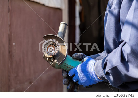A professional technician holds a portable angle grinder with a wire brush attachment to perform effective metal surface preparation and rust removal tasks within a busy industrial workshop 139638743