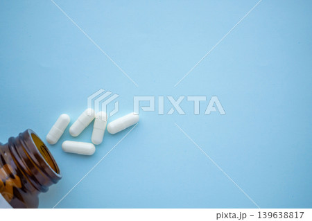 medicine pills capsule spilling out of bottle on blue background medicine pills capsule spilling out of bottle on blue background 139638817