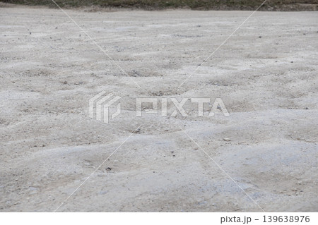 An unpaved dirt road surface with wavy ripples and textured soil patterns illustrates the rough terrain conditions for transportation, rugged travel, and infrastructure maintenance in rural areas An unpaved dirt road surface with wavy ripples and textured soil patterns illustrates the rough terrain conditions for transportation, rugged travel, and infrastructure maintenance in rural areas 139638976