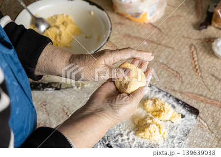 An elderly woman shapes fresh cottage cheese pancakes by hand in a rustic kitchen, carefully preparing traditional dough for a warm, homemade breakfast in a nurturing culinary home environment An elderly woman shapes fresh cottage cheese pancakes by hand in a rustic kitchen, carefully preparing traditional dough for a warm, homemade breakfast in a nurturing culinary home environment 139639038
