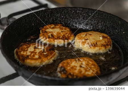Syrniki frying in a hot cast iron skillet, showcasing traditional curd pancakes golden brown during cooking process for breakfast culinary concepts in a home kitchen environment for food blog Syrniki frying in a hot cast iron skillet, showcasing traditional curd pancakes golden brown during cooking process for breakfast culinary concepts in a home kitchen environment for food blog 139639044