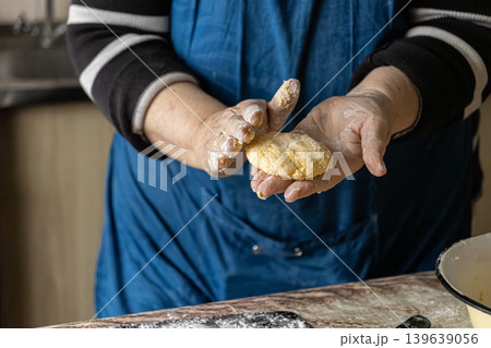 Woman shaping cottage cheese pancakes with floury hands, preparing traditional syrniki for a healthy home cooked breakfast in a rustic kitchen setting, capturing culinary arts and tradition 139639056