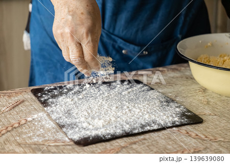 An elderly person carefully dusts flour over a dark surface to prepare fresh dough for baking bread, capturing authentic traditional culinary methods and the true joy of homemade kitchen cooking An elderly person carefully dusts flour over a dark surface to prepare fresh dough for baking bread, capturing authentic traditional culinary methods and the true joy of homemade kitchen cooking 139639080