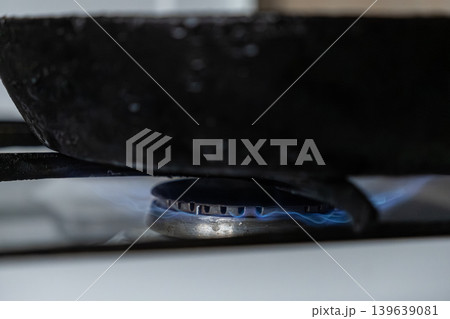 Cast iron frying pan resting on a gas stove burner with blue flame, representing home cooking, preparation of healthy food, professional culinary art, and sustainable lifestyle daily routine Cast iron frying pan resting on a gas stove burner with blue flame, representing home cooking, preparation of healthy food, professional culinary art, and sustainable lifestyle daily routine 139639081