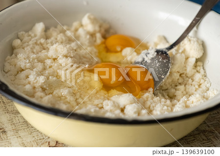 Fresh eggs combined with soft cottage cheese in a ceramic mixing bowl, preparing healthy ingredients for traditional homemade pastry or morning breakfast recipes in a bright kitchen setting Fresh eggs combined with soft cottage cheese in a ceramic mixing bowl, preparing healthy ingredients for traditional homemade pastry or morning breakfast recipes in a bright kitchen setting 139639100