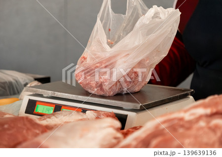 Raw meat in plastic bag being weighed on digital scale at butcher shop counter for purchase, highlighting food retail service and market industry quality control standards in local business 139639136
