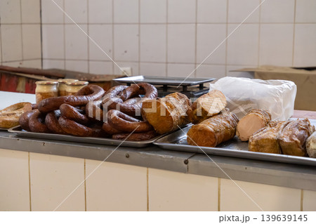 Assortment of traditional smoked sausages and cured meat products displayed on metal trays at a butcher shop counter, representing artisanal craftsmanship and authentic rustic culinary heritage 139639145