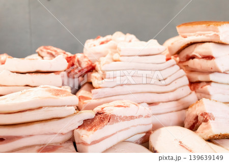 Raw pork fat pieces stacked on a market counter, representing fresh butchery products for cooking traditional savory dishes and culinary preparation in a commercial food retail environment 139639149