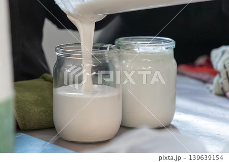 Fresh sour cream is poured into glass jars during kitchen preparation to capture the smooth texture and natural process of homemade dairy production for professional culinary and home use Fresh sour cream is poured into glass jars during kitchen preparation to capture the smooth texture and natural process of homemade dairy production for professional culinary and home use 139639154