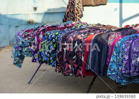 Display table with folded colorful patterned textiles and casual garments at an outdoor market stall, highlighting small business retail activity and local trade in a casual summer setting 139639160