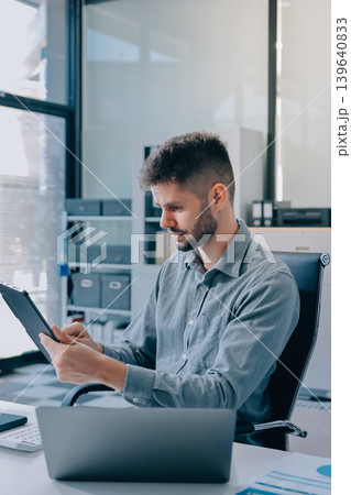 Tired worker. A tired businessman works in the evening. A man in office clothes is holding his temples. Problems in business. The businessman is trying to solve the problems that have arisen. 139640833
