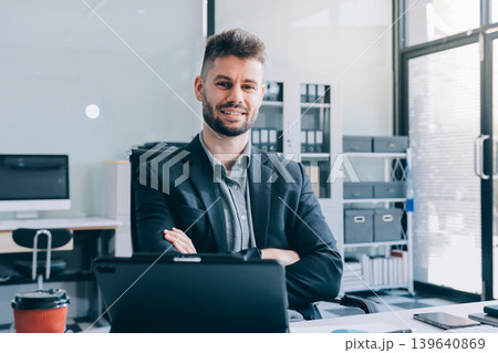 Smiling businessman in suit works on laptop in bright modern office Smiling businessman in suit works on laptop in bright modern office 139640869