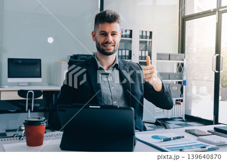 Smiling businessman in suit works on laptop in bright modern office Smiling businessman in suit works on laptop in bright modern office 139640870