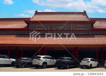 Traditional Chinese temple architecture with intricate colorful patterns and red pillars, featuring a parking lot with modern cars in Thailand. A blend of ancient culture and modern life Traditional Chinese temple architecture with intricate colorful patterns and red pillars, featuring a parking lot with modern cars in Thailand. A blend of ancient culture and modern life 139641054