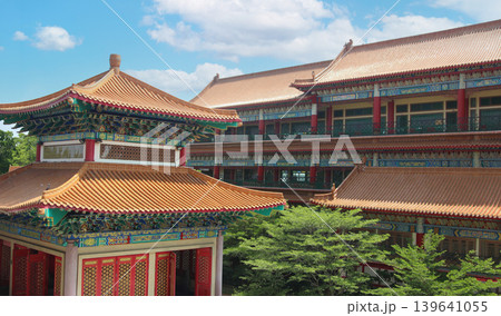 traditional Chinese temple architecture featuring ornate roof patterns, red windows, and colorful decorations against a clear sky with copy space for design. 139641055