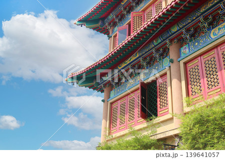 traditional Chinese temple architecture featuring ornate roof patterns, red windows, and colorful decorations against a clear sky with copy space for design. 139641057