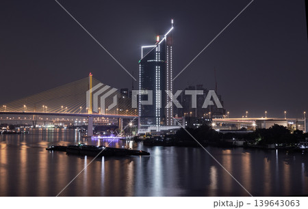 A modern skyscraper and an illuminated suspension bridge the golden Thotsamarachan Bridge (Rama IX Bridge) the night sky, mirroring their brilliant lights across the dark, undulating surface of the A modern skyscraper and an illuminated suspension bridge the golden Thotsamarachan Bridge (Rama IX Bridge) the night sky, mirroring their brilliant lights across the dark, undulating surface of the 139643063