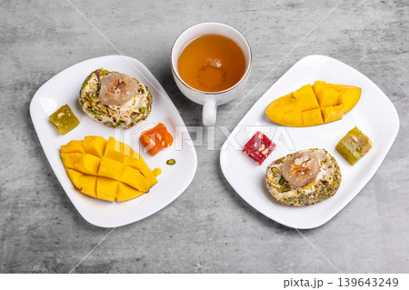 Cup of tea and halva, sweets and a mango fruit on the white plates. Cup of tea and halva, sweets and a mango fruit on the white plates. 139643249