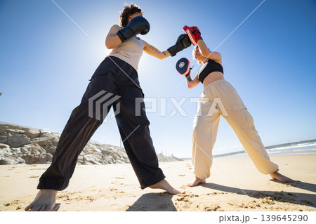 Women boxing training on sunny beach with focus mitts Women boxing training on sunny beach with focus mitts 139645290