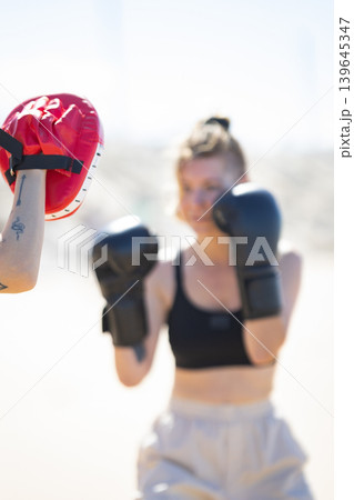 Woman training boxing striking focus mitt outdoors Woman training boxing striking focus mitt outdoors 139645347