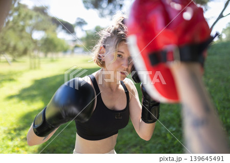 Woman boxer training with focus mitt outdoors Woman boxer training with focus mitt outdoors 139645491
