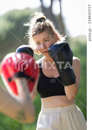 Woman training boxing with punch mitts outdoors Woman training boxing with punch mitts outdoors 139645557