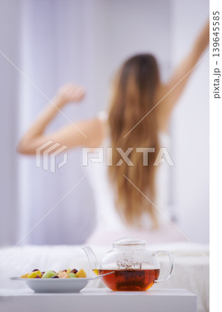 Breakfast, tea and woman in bedroom, stretching with fruit salad for good diet and nutrition. Healthy food, herbal drink and wake up, girl on bed getting ready to start day in home or hotel from back 139645585