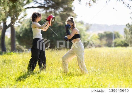 Young women training boxing outdoors using punch pads Young women training boxing outdoors using punch pads 139645640