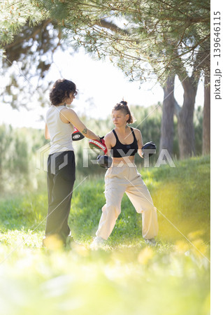 Women training boxing hitting punch mitts outdoors Women training boxing hitting punch mitts outdoors 139646115