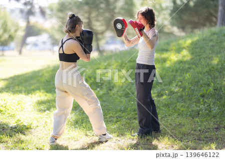 Women training boxing with focus mitts outdoors Women training boxing with focus mitts outdoors 139646122
