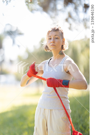 Young woman wrapping hands with red boxing wraps outdoors Young woman wrapping hands with red boxing wraps outdoors 139646190