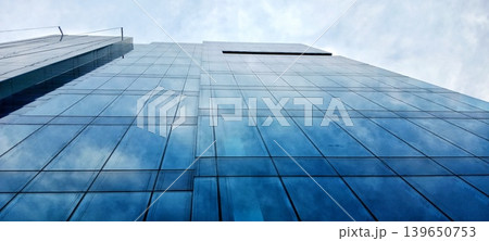 Low angle of blue glass facade of a modern, symmetrical office building Low angle of blue glass facade of a modern, symmetrical office building 139650753