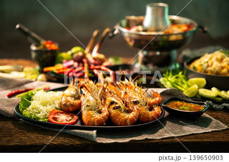 Close up grilled river prawns with spicy seafood dipping sauce, Thai hot pot and fresh herbs on rustic wooden table, authentic Asian seafood cuisine concept for restaurant and food advertising Close up grilled river prawns with spicy seafood dipping sauce, Thai hot pot and fresh herbs on rustic wooden table, authentic Asian seafood cuisine concept for restaurant and food advertising 139650903
