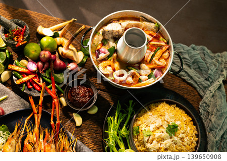 Top view of authentic Thai seafood hot pot with crab fried rice, grilled river prawns, herbs and spicy dipping sauce on rustic wooden table, traditional Asian seafood cuisine concept Top view of authentic Thai seafood hot pot with crab fried rice, grilled river prawns, herbs and spicy dipping sauce on rustic wooden table, traditional Asian seafood cuisine concept 139650908