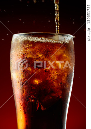 Sparkling cola is poured into a misted glass with ice. 139651725