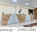 Modern reception desk showcases a wooden finish with geometric patterns in a bright office space, complemented by indoor plants and decorative items 139651882
