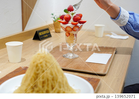 カフェで新鮮ないちごパフェをスプーンで掬う様子、手前にモンブランのデザート 139652071