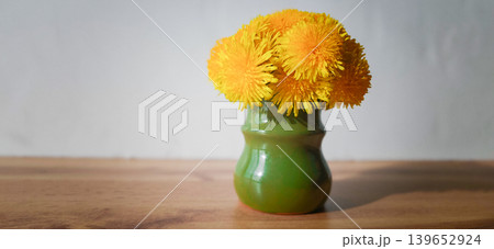 Bright yellow dandelions in a green vase on a wooden table in sunlight Bright yellow dandelions in a green vase on a wooden table in sunlight 139652924