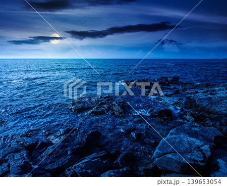 sea coast with stones and boulders at night. view of beach with rock in seaweed. full moon over dynamic cloudscape on the sky above horizon. mysterious summer vacations background concept sea coast with stones and boulders at night. view of beach with rock in seaweed. full moon over dynamic cloudscape on the sky above horizon. mysterious summer vacations background concept 139653054