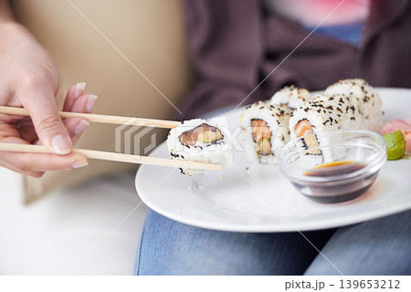 Hands, sushi plate and chopsticks in closeup, home or eating for wellness, diet or meal with soy sauce. Hungry person, fish and dish at lunch, nutrition or snack for takeaway food, house or apartment 139653212