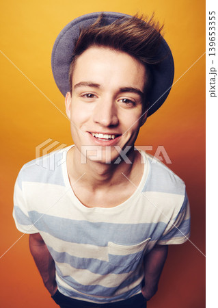Portrait, smile and man with fashion, stylish clothes and cool guy on an orange studio background. Face, happy person or model with accessory, student and aesthetic with casual outfit, trendy and hat 139653355