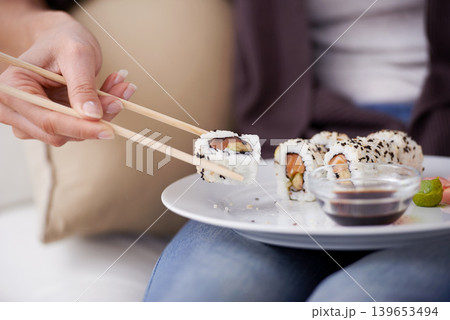 Hands, sushi plate and chopsticks in home, closeup or eating for wellness, diet or meal with soy sauce. Hungry person, fish and dish at lunch, nutrition or snack for takeaway food, house or apartment Hands, sushi plate and chopsticks in home, closeup or eating for wellness, diet or meal with soy sauce. Hungry person, fish and dish at lunch, nutrition or snack for takeaway food, house or apartment 139653494