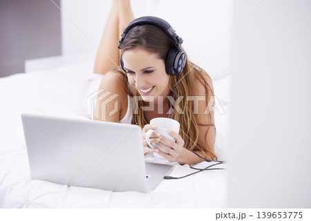 Woman, bedroom and coffee on laptop for listening, watching and video streaming in headphones at home. Young person relax on bed with computer for morning news, social media or happy audio or podcast Woman, bedroom and coffee on laptop for listening, watching and video streaming in headphones at home. Young person relax on bed with computer for morning news, social media or happy audio or podcast 139653775