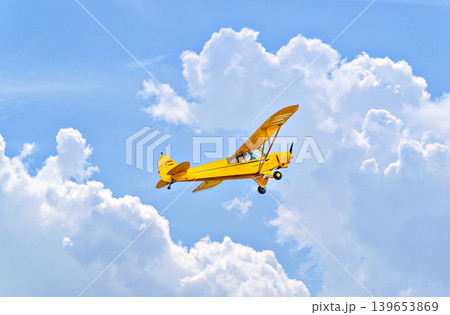 A yellow single-engine ultralight aircraft flying in a blue sky with white clouds. A yellow single-engine ultralight aircraft flying in a blue sky with white clouds. 139653869