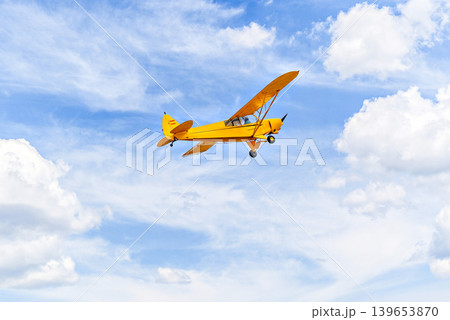 A yellow single-engine ultralight aircraft flying in a blue sky with white clouds. 139653870