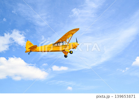 A yellow single-engine ultralight aircraft flying in a blue sky with white clouds. A yellow single-engine ultralight aircraft flying in a blue sky with white clouds. 139653871